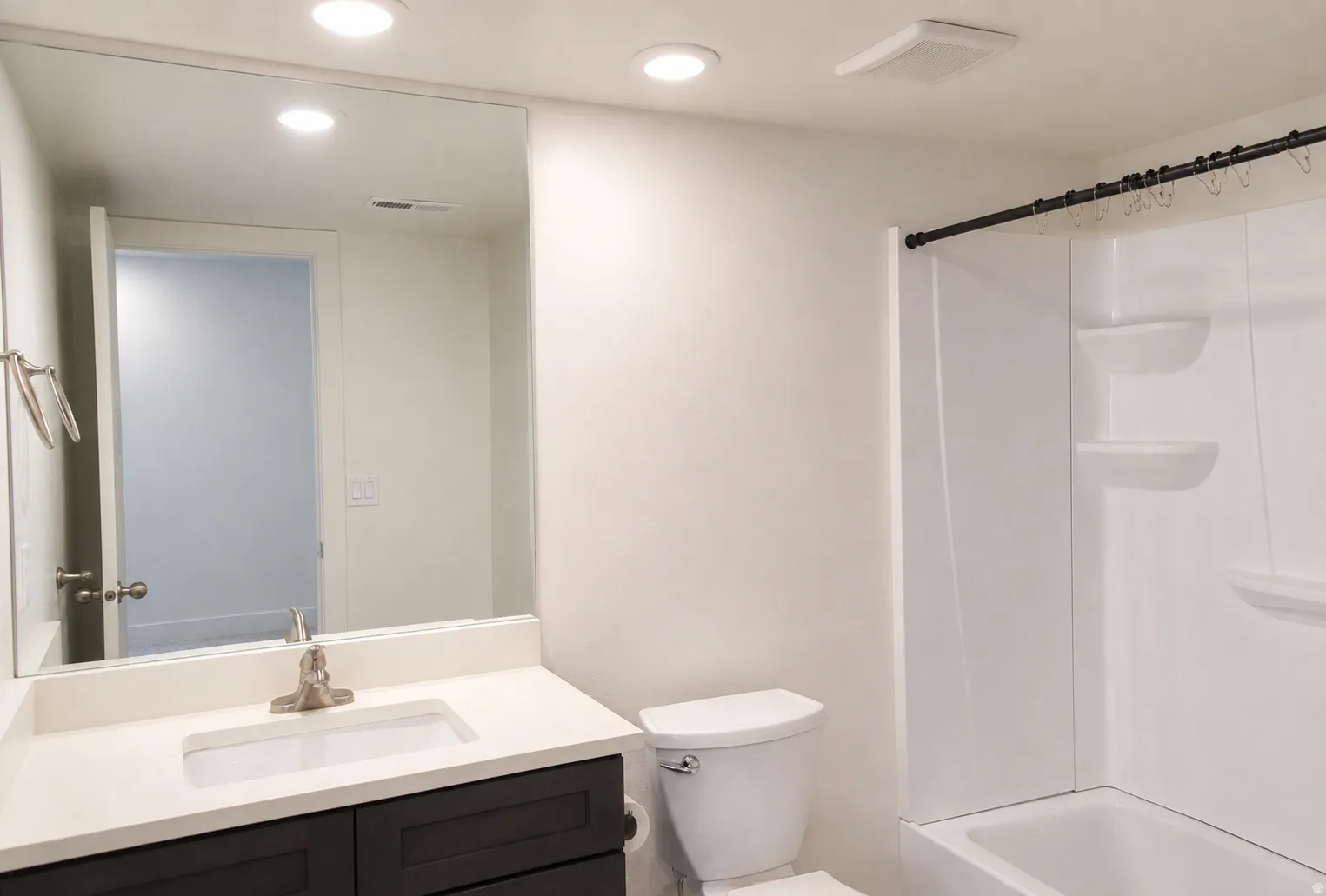 White vanity with a brushed nickel faucet, large wall mirror, and recessed lighting