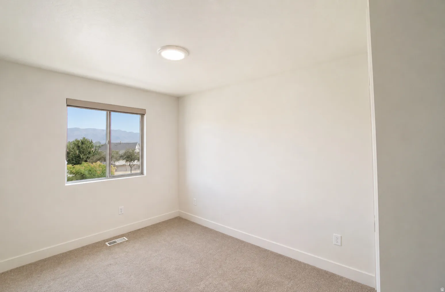 Neutral wall paint, window with roller shade, carpeted flooring, and a flush mount ceiling light