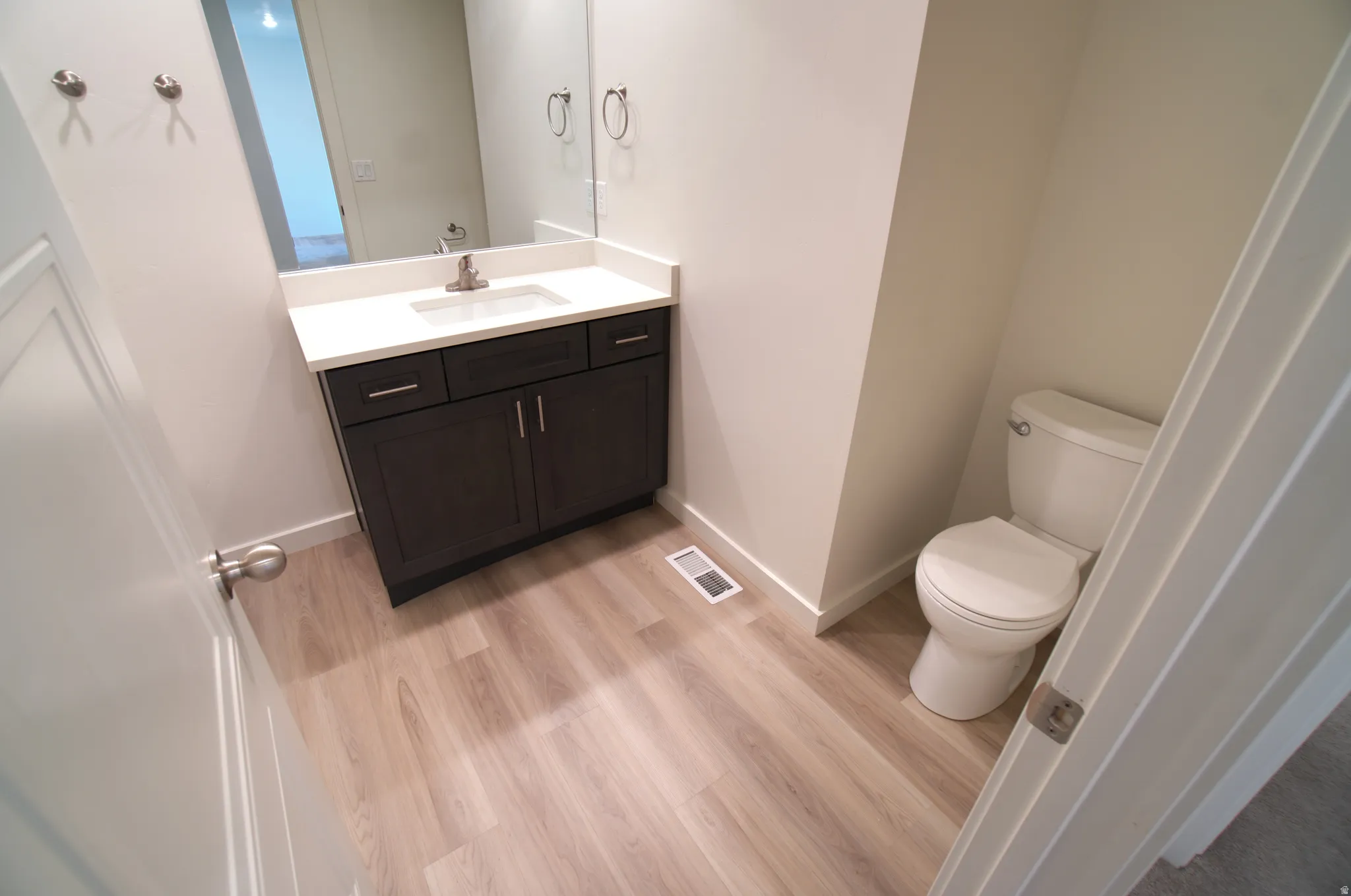 Modern vanity with a white countertop and dark wood-finish cabinetry, under-mount sink, brushed nickel faucet, and coordinating wall mirror