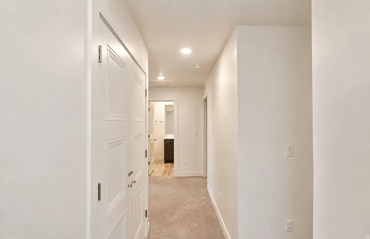 Recessed lighting illuminates a hallway with carpet flooring and white walls