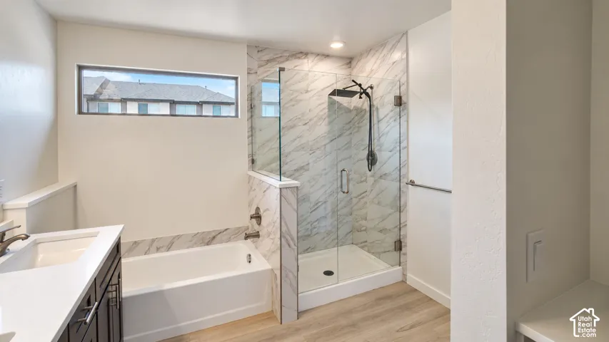 Bathroom featuring a deep-soaking tub, glass-enclosed walk-in shower with floor-to-ceiling tile surround, dark cabinetry with light-toned countertop, and wood-finish flooring