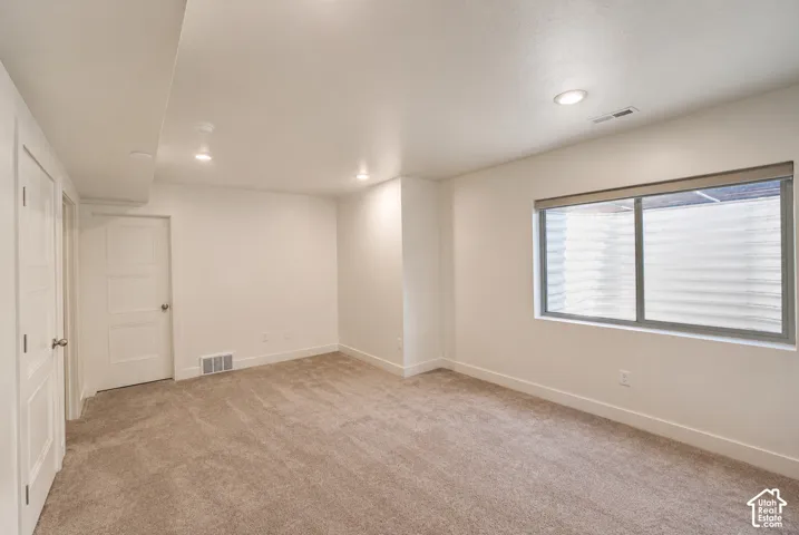Recessed ceiling lighting, textured carpet flooring, white painted walls, and a large window with privacy blinds