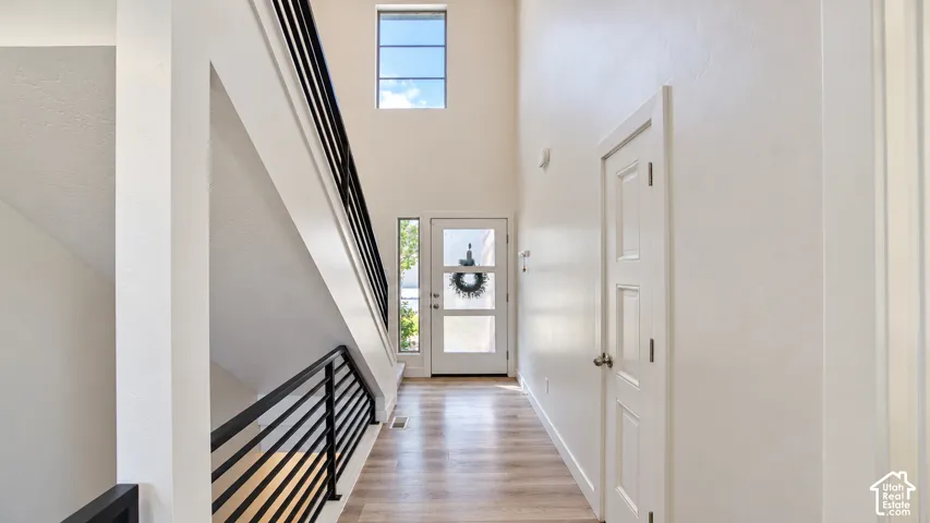 Entryway featuring high ceilings, wood-finish flooring, a contemporary staircase with black horizontal metal railings, and a door with glass panels