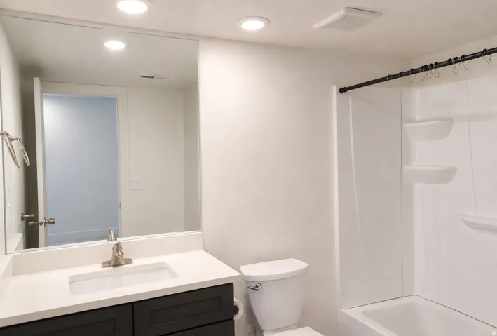 White vanity with a brushed nickel faucet, large wall mirror, and recessed lighting