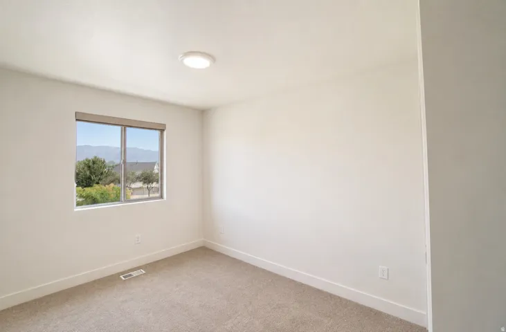Neutral wall paint, window with roller shade, carpeted flooring, and a flush mount ceiling light
