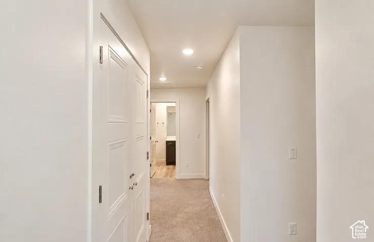 Recessed lighting illuminates a hallway with carpet flooring and white walls