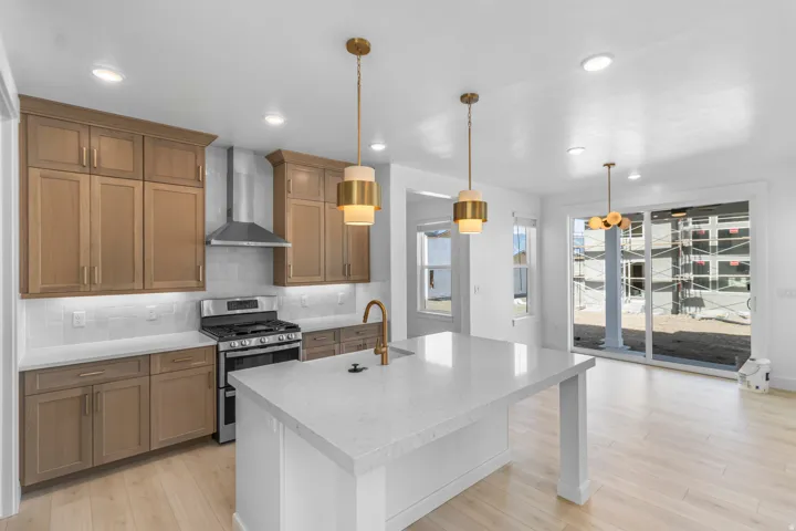 Modern kitchen featuring a central island with a light-toned countertop, stainless steel appliances, light wood-finish cabinetry, recessed lighting, and pendant fixtures