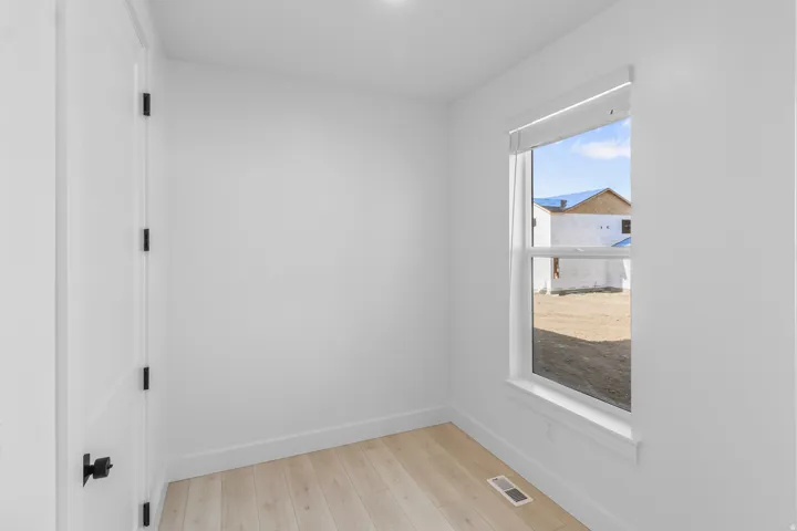 White painted walls with light wood-finish flooring, featuring a window with white trim and a white door with black hardware