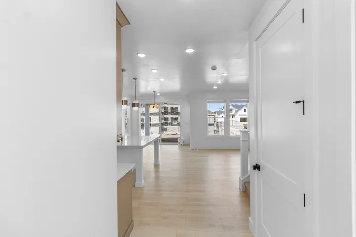Recessed lighting, light wood-finish flooring, white walls, white interior door, and a kitchen island with pendant lighting