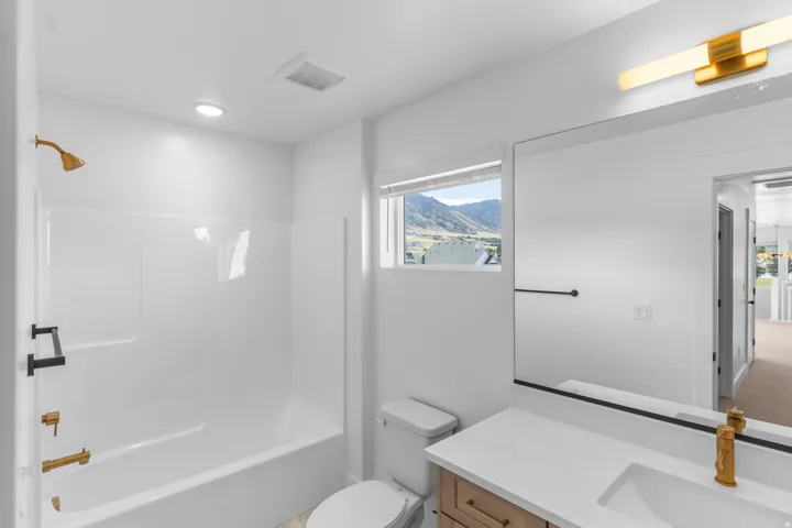 White bathtub with brass-finish fixtures, a large vanity mirror, and a gold-toned bar light fixture
