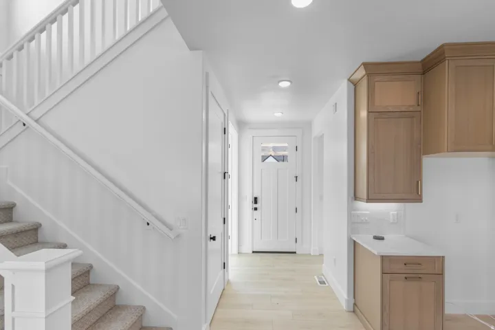 White shaker-style front door with frosted glass insert, wood-finish flooring, recessed lighting, and light wood cabinetry with under-cabinet lighting