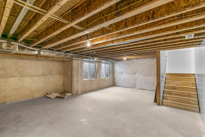 Unfinished basement with exposed ceiling joists, concrete flooring, and bare wood stairs