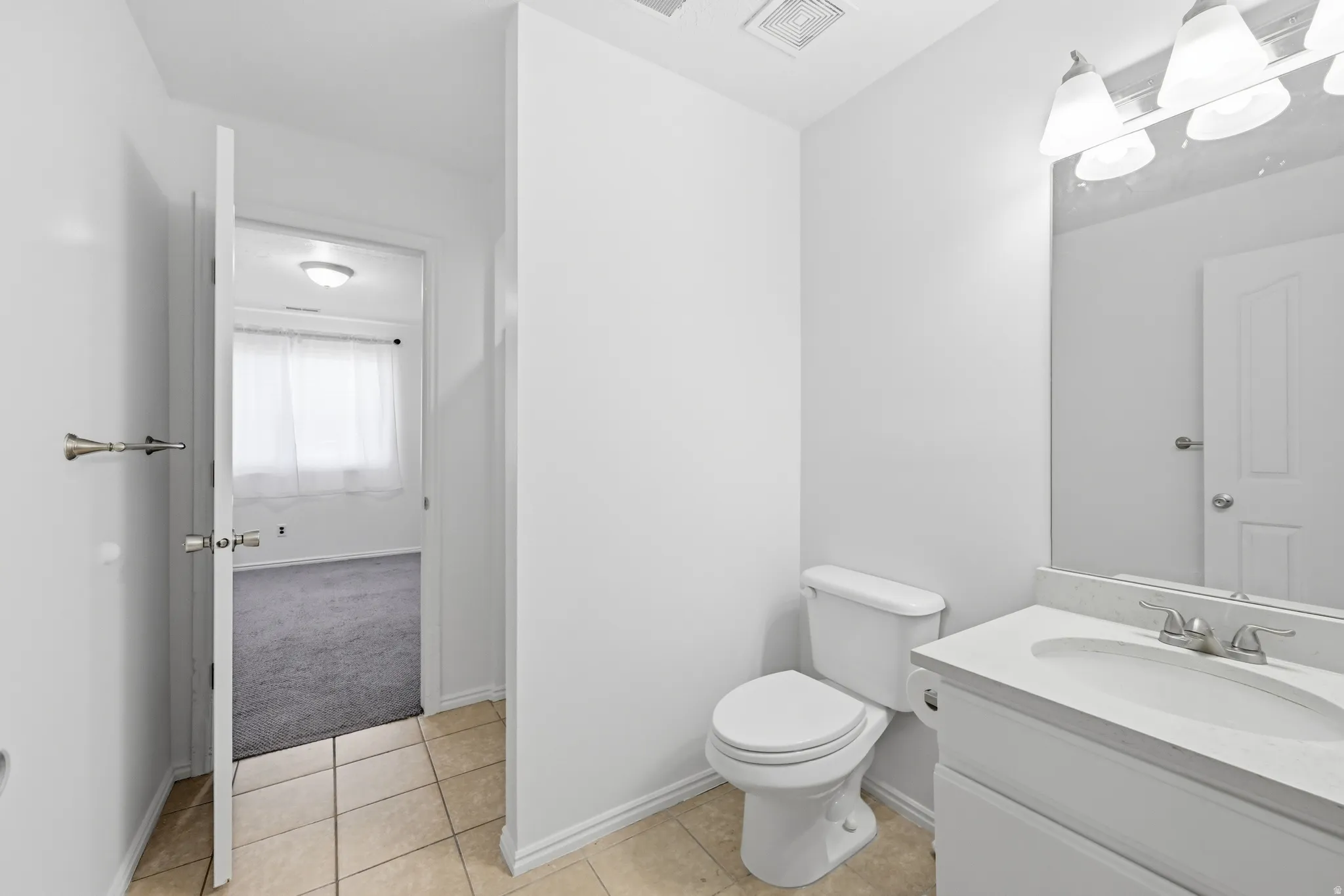 Neutral-toned tile flooring, white vanity with integrated sink, chrome faucet, and overhead vanity lighting