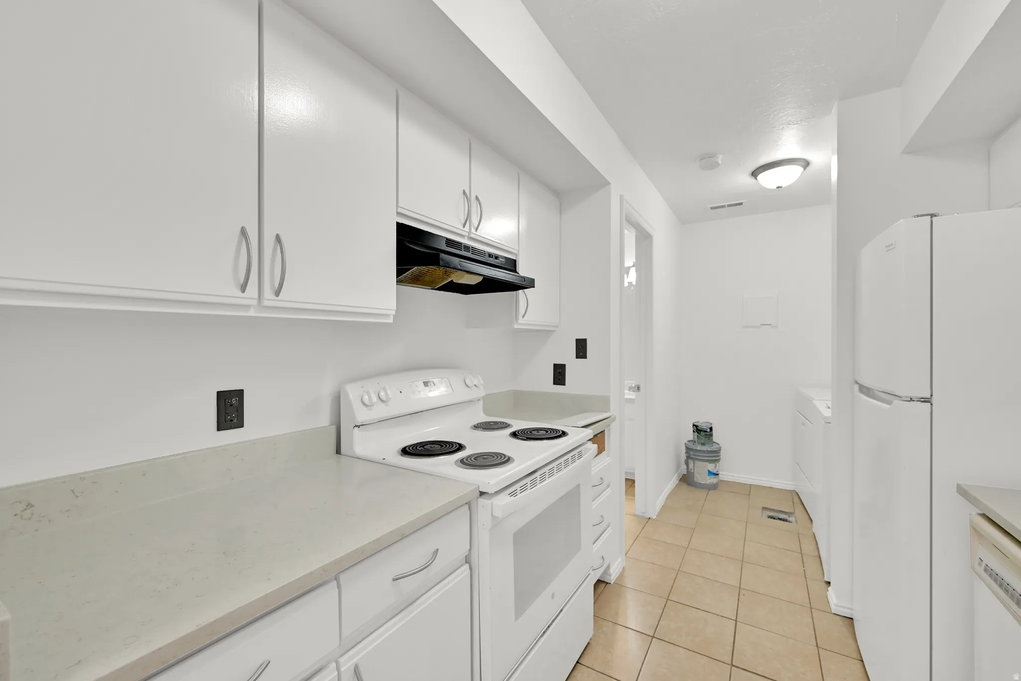 White cabinetry, light countertops, white electric range, white refrigerator, and tiled flooring