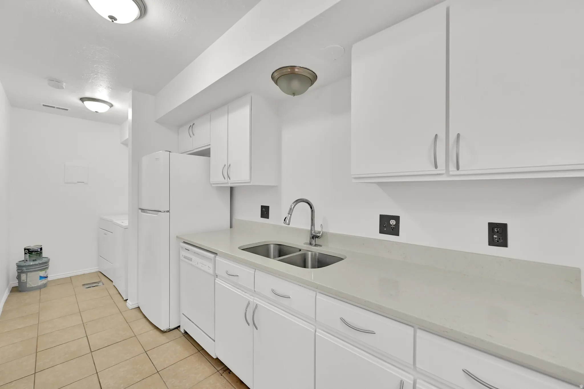 White cabinetry with brushed nickel hardware, stainless steel double basin sink, light-toned countertop, and tile flooring