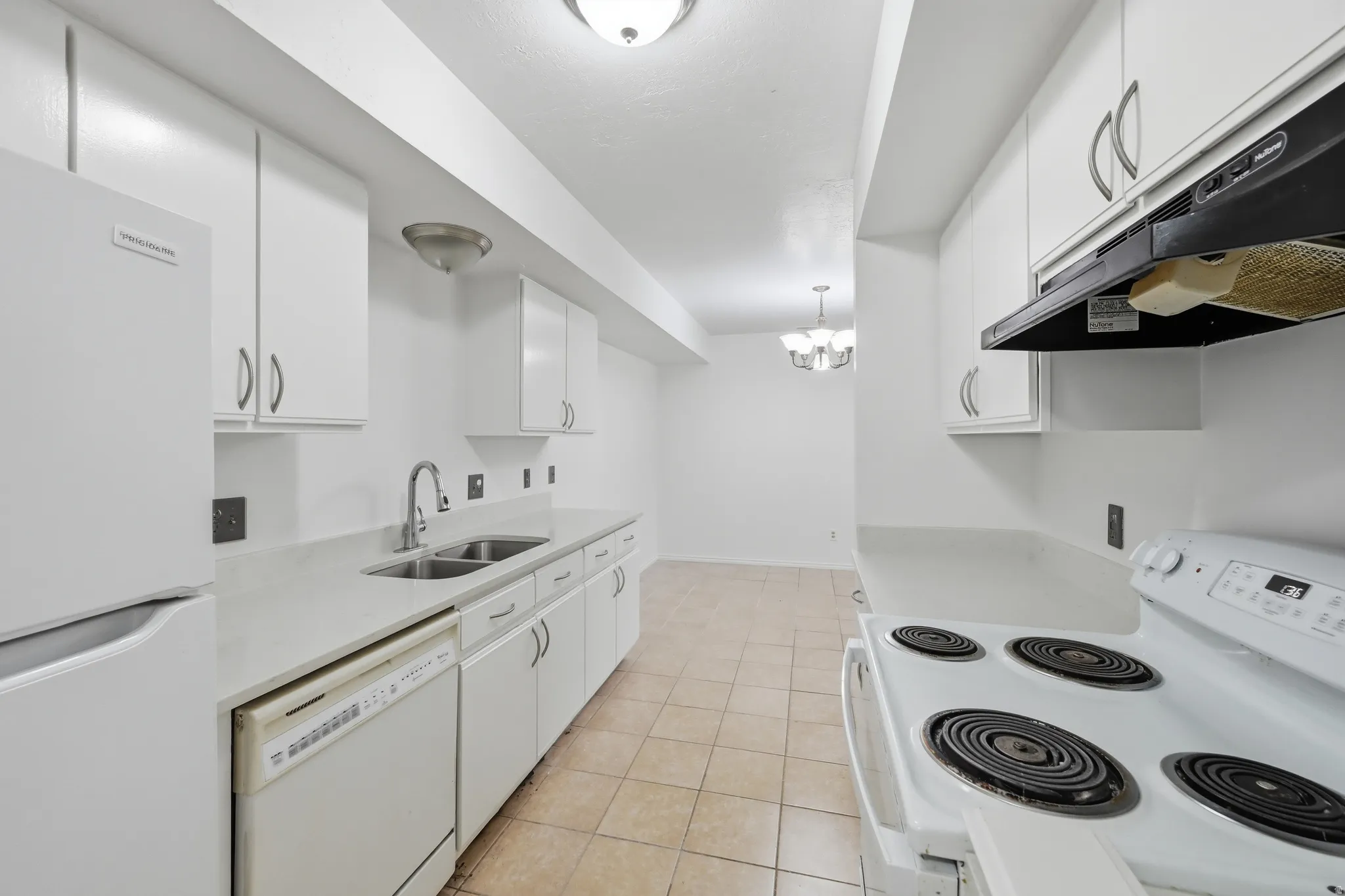 White cabinetry with silver hardware, dual basin stainless steel sink, included white appliances, light-toned tiled flooring, and recessed ceiling lighting