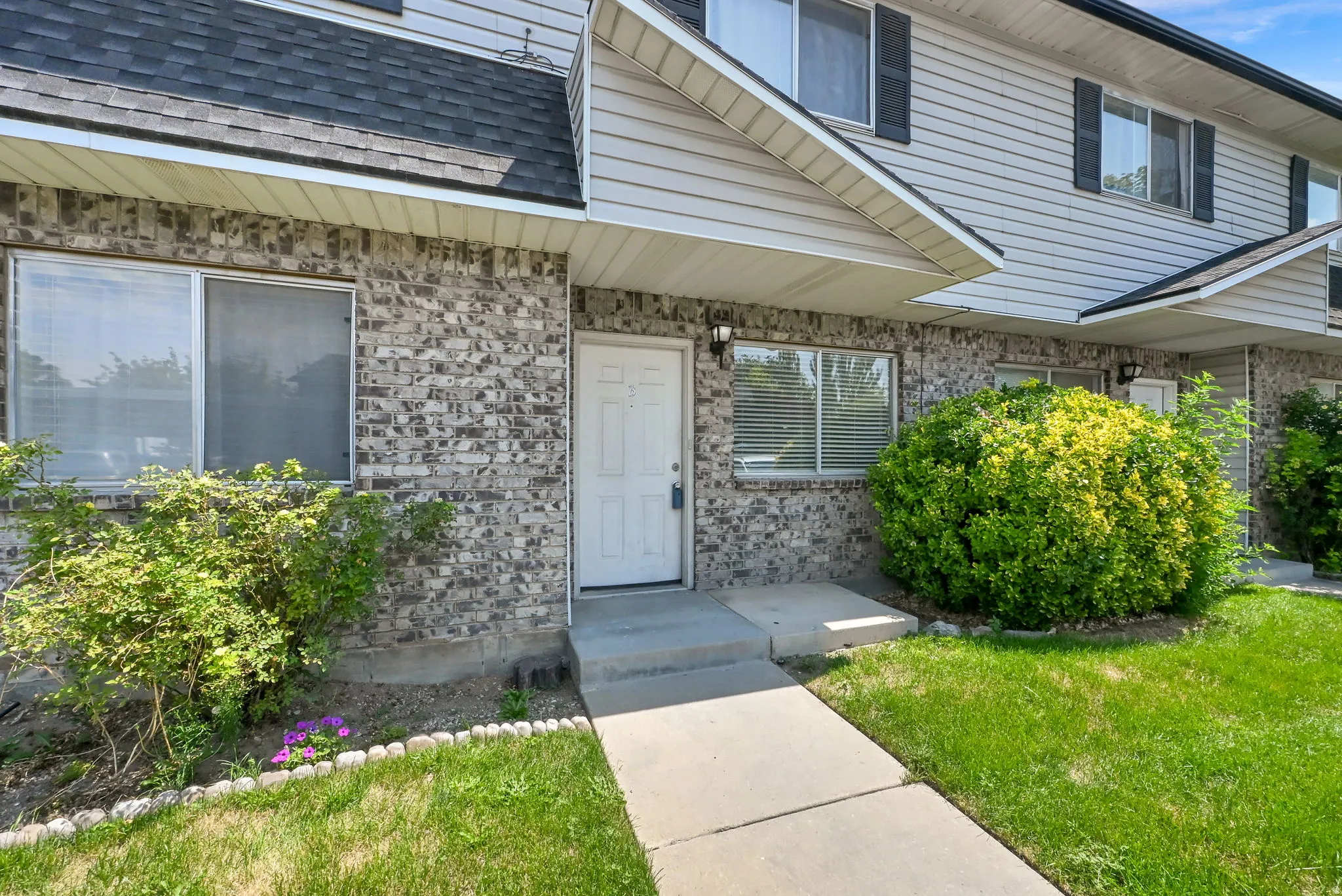 Brick facade with siding accents, gabled roofline, front entry door, concrete walkway, and manicured landscaping
