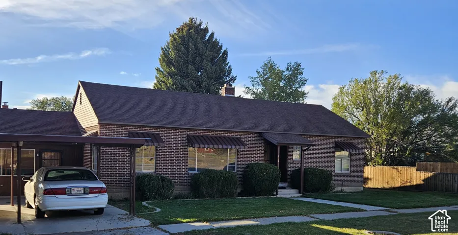 Brick exterior residence featuring a carport, awnings, mature front landscaping, a paved front walkway