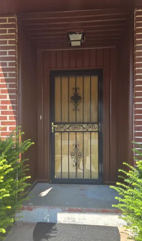 Front dark brown wood-paneled entry, featuring a decorative security door and an overhead light fixture