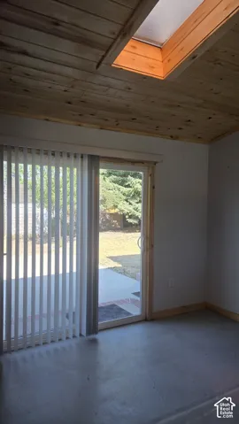 Salon. Wood-paneled ceiling with an integrated skylight, sliding glass door, and concrete flooring