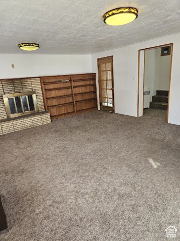 Carpeted flooring, built-in shelving, fireplace with brick surround, and a paneled door