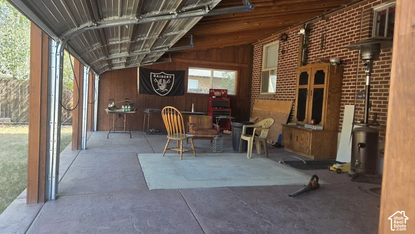 Covered patio with stamped concrete flooring, exposed brick wall, wood-paneled ceiling, and roll-up garage door access