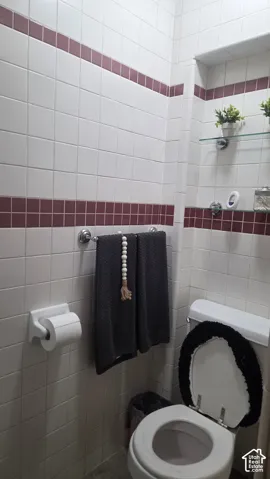 2nd bathrm, with white wall tile & accenting maroon tile bands is located next to 2nd bedrm