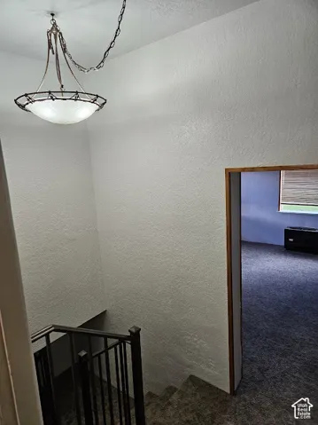 Staircase with metal railings, overhead chandelier, and textured wall finishes