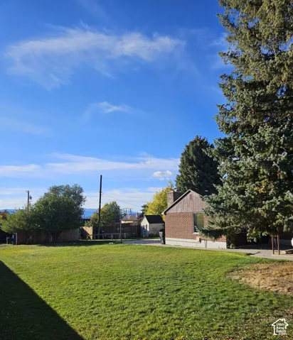 South side with expansive green lawn with mature evergreen trees and a brick and wood-sided structure