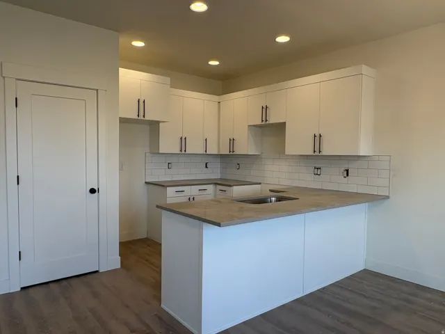 Kitchen featuring a central island with an integrated sink, white shaker-style cabinetry with matte black hardware, subway tile backsplash, and wood-finish flooring