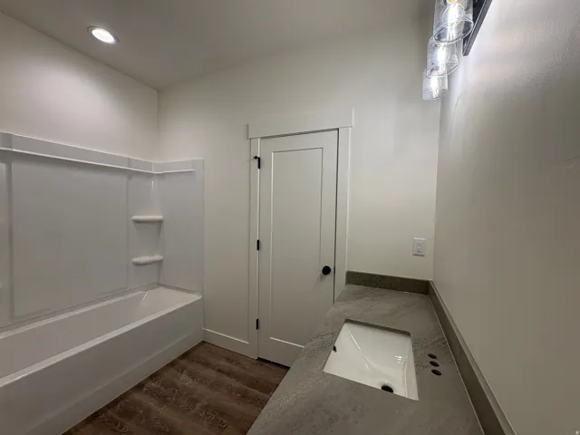 Built-in bathtub with integrated shelving, recessed ceiling lighting, wood-finish flooring, vanity with integrated sink, and a modern light fixture