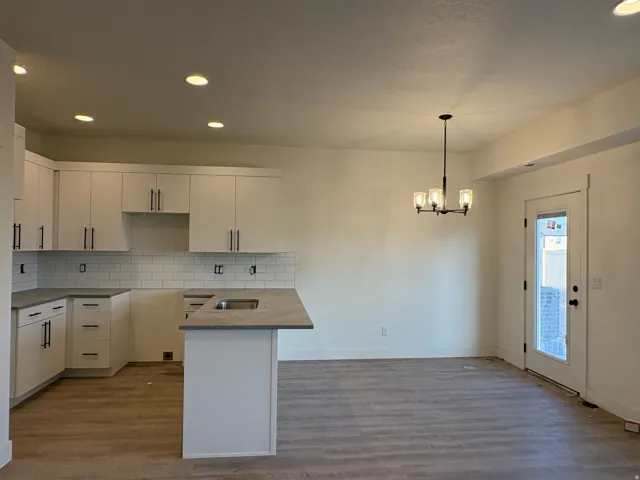White shaker cabinetry, subway tile backsplash, dark countertops, wood-finish flooring, and recessed lighting