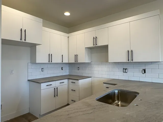 White flat-panel cabinetry with matte black hardware, subway tile backsplash, and light-toned countertops with an undermount stainless steel sink