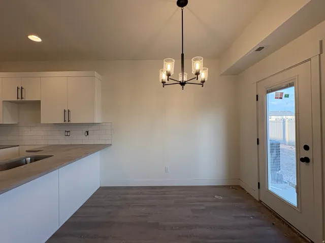 Recessed and chandelier lighting, wood-finish flooring, white cabinetry with dark hardware, subway tile backsplash, and a glass-paned exterior door