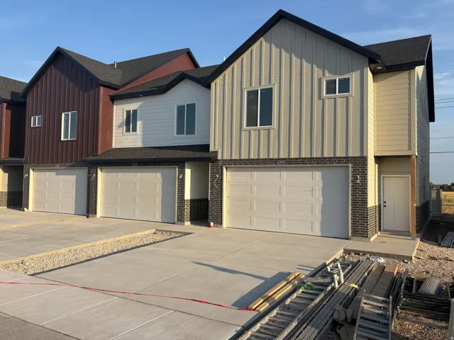 Contemporary townhome exterior featuring multi-toned vertical siding, dark brick accents, a dark shingle roof, and a panel garage door