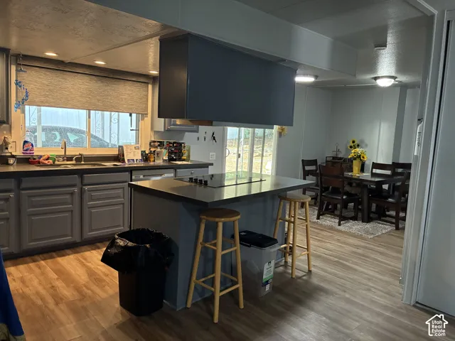 Kitchen featuring wood-finish flooring, gray cabinetry, a central island with a cooktop, and an integrated dining area with sliding glass doors