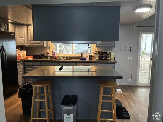 Kitchen featuring gray cabinetry, a black refrigerator, a stainless steel sink, wood-finish flooring, and a sliding glass door
