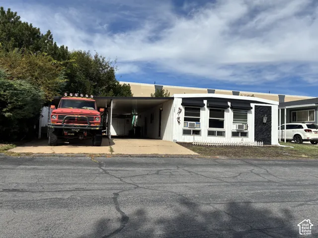 Carport parking, white siding, black window awnings, and an exterior wall light fixture