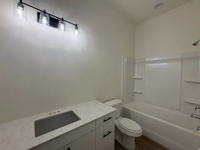 Vanity with an integrated rectangular sink, white countertop, white cabinetry with black hardware, modern black track lighting, and a white bathtub with shower surround