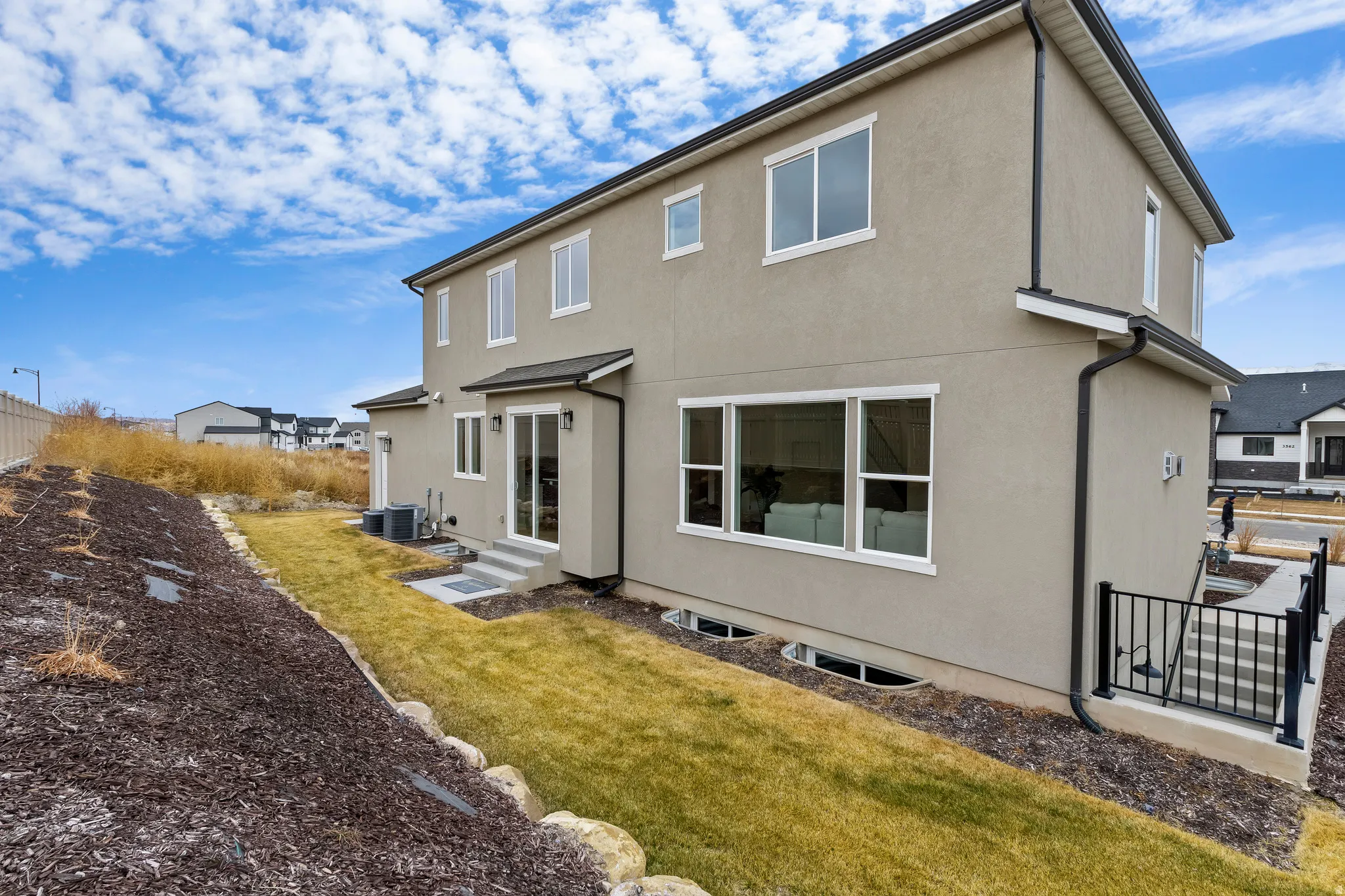 Stucco exterior with multiple windows, leading to a lower level patio with black railing