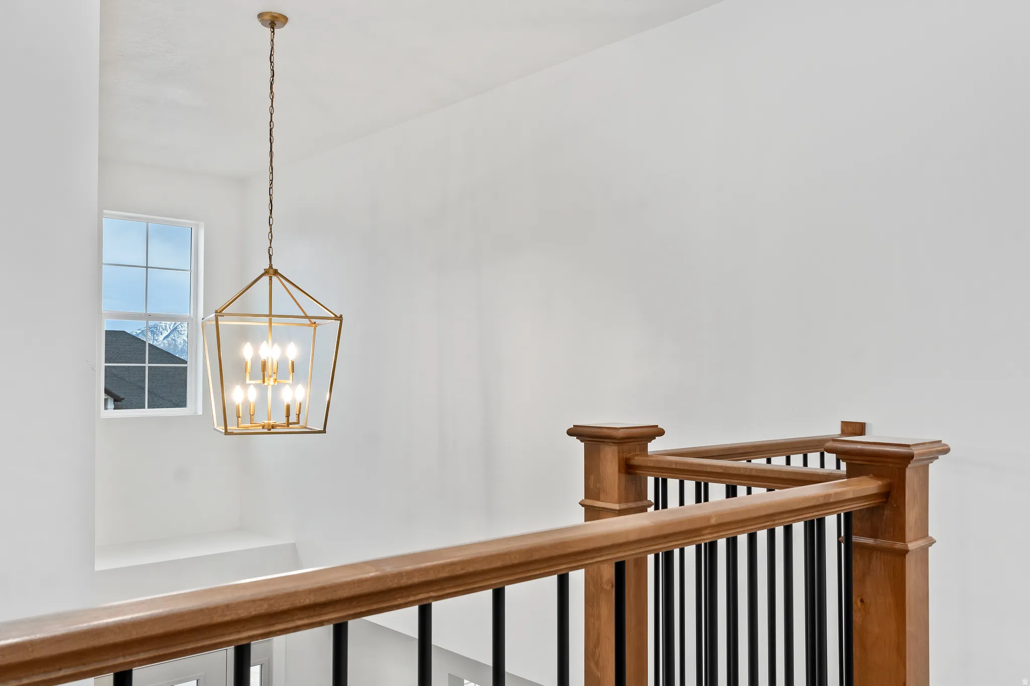 Two-story ceiling, large window, linear chandelier, wood-finish railing, and black metal balusters