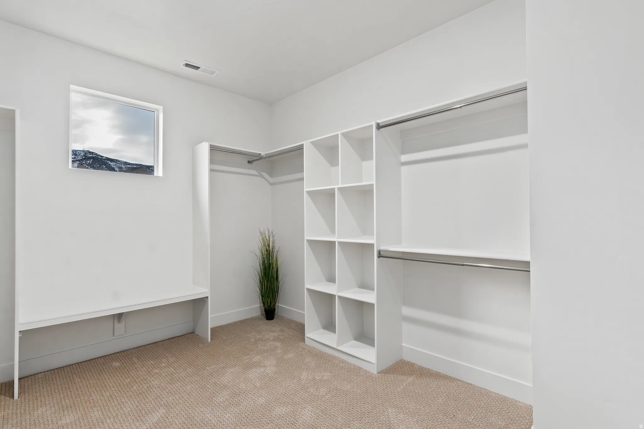 Built-in custom shelving, integrated hanging rods, built-in bench, neutral carpeting, and a window with mountain scenery