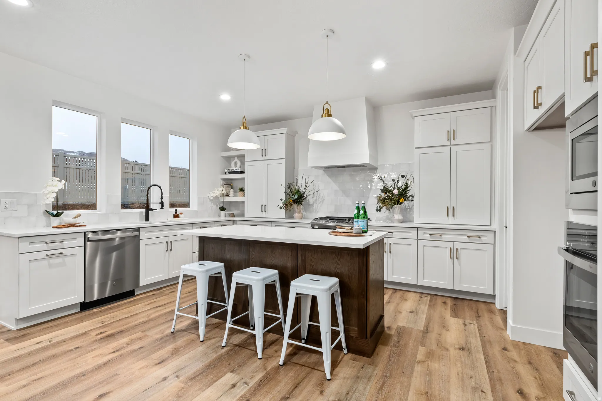 White cabinetry with gold-tone hardware, wood-finish flooring, stainless steel appliances, a center island with a white countertop, and recessed lighting