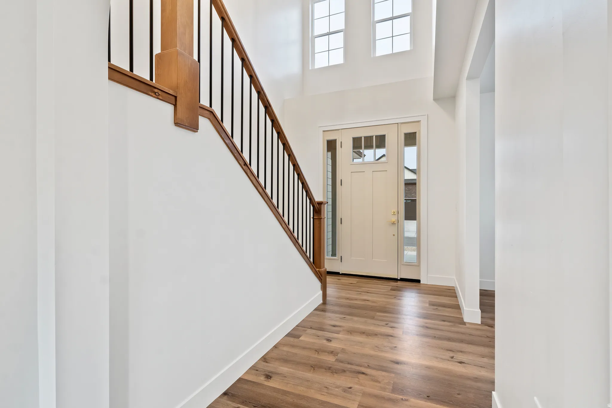 Entryway featuring wood-finish flooring, a light-colored main door with sidelights, and a staircase with a wood railing and black balusters