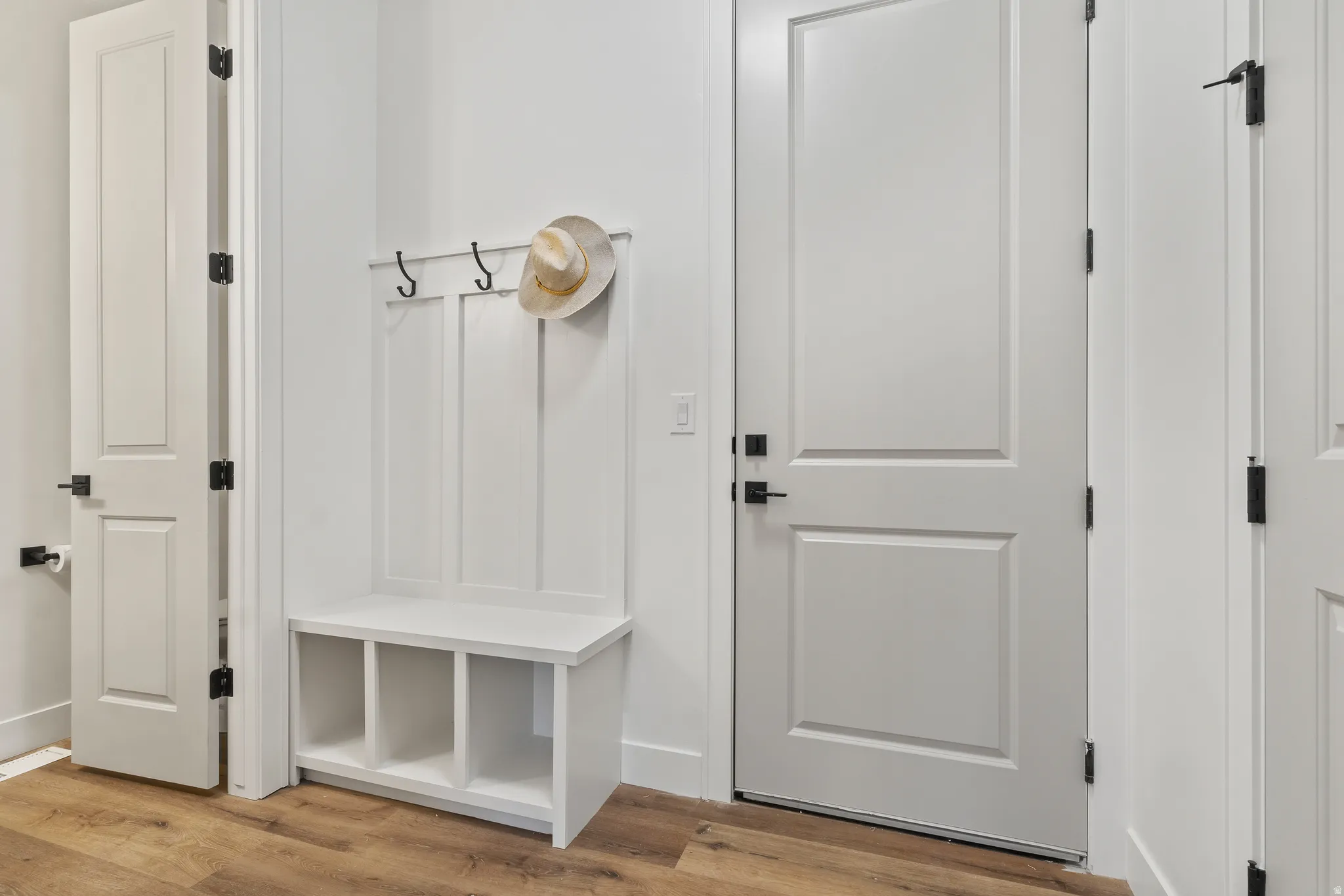 Built-in white storage bench with open cubbies, wall-mounted coat hooks, and durable wood-finish flooring