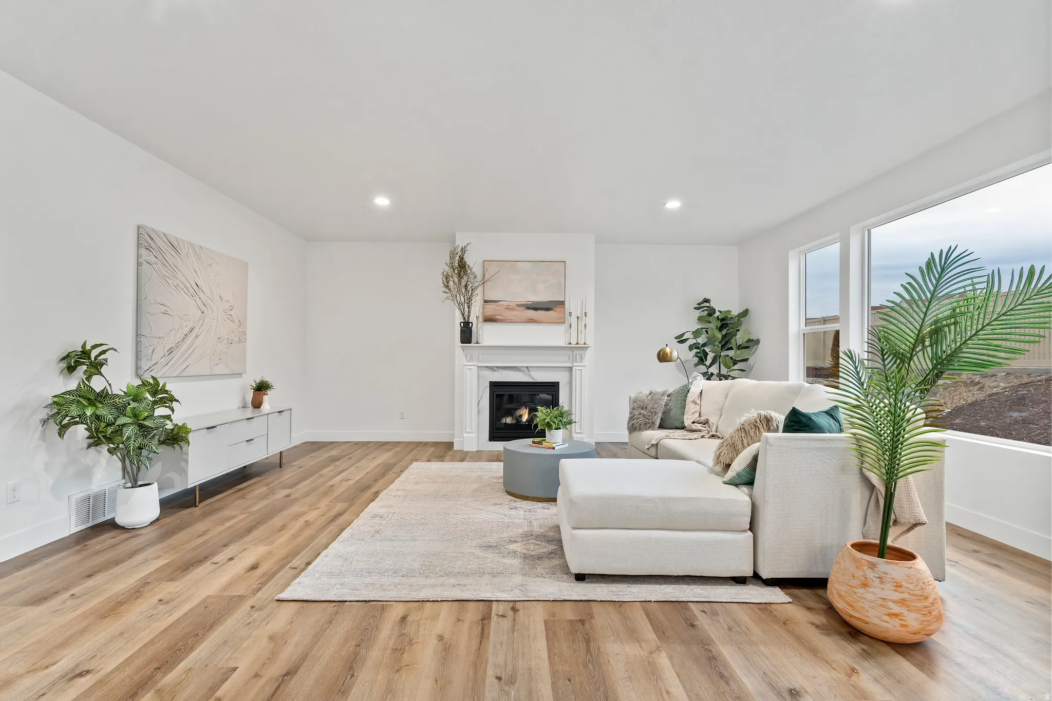 Recessed lighting, wood-finish flooring, white walls, and a fireplace with a white mantel and hearth