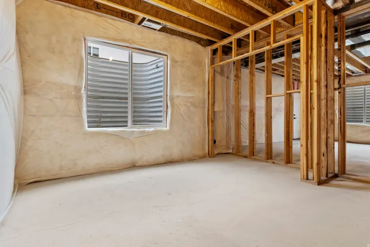 Unfinished basement featuring exposed wood framing, concrete flooring, a sliding window, and exposed ceiling joists