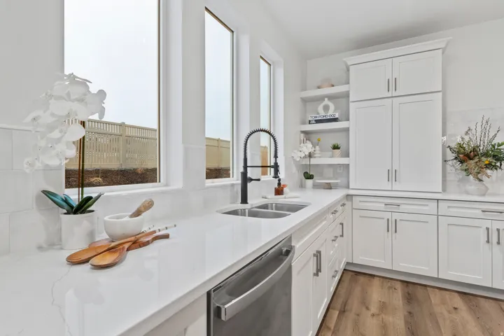 White shaker cabinetry, light-toned countertops, subway tile backsplash, stainless steel dishwasher, and wood-finish flooring