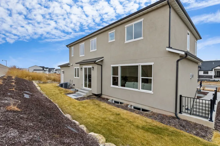 Stucco exterior with multiple windows, leading to a lower level patio with black railing