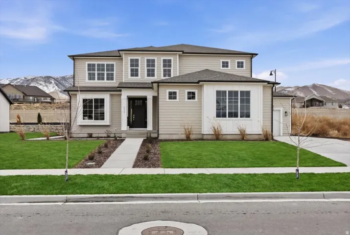 Two-story residence featuring light-toned siding, a dark roof, a two-car garage, and a concrete pathway leading to the entry